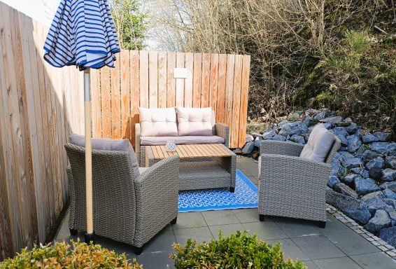 Gemütliche Sitzecke mit Rattanmöbeln, Sonnenschirm und blauem Teppich im Freien.