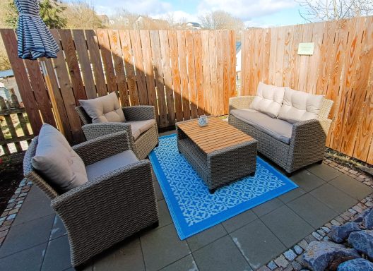 Gemütliche Sitzecke mit Sofas und Tisch auf gefliestem Boden, umgeben von Holzzaun.